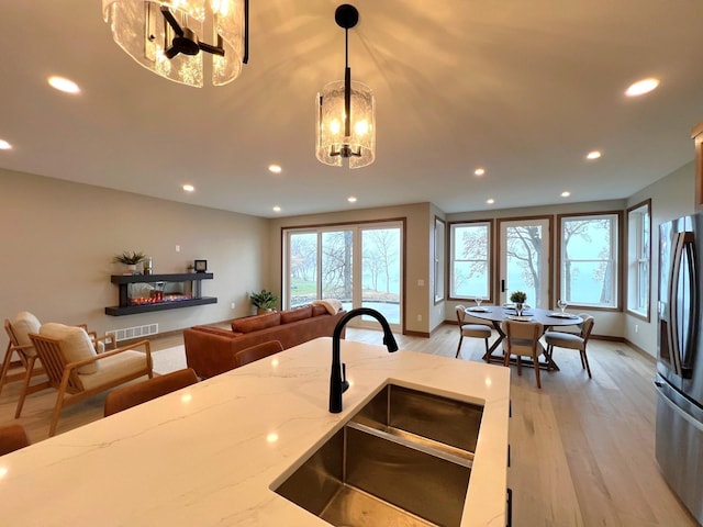 kitchen with decorative light fixtures, sink, stainless steel fridge, light stone counters, and light wood-type flooring