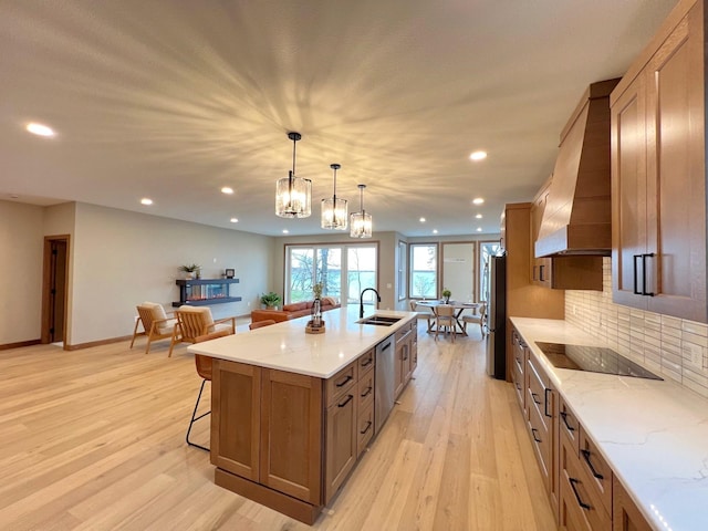 kitchen with a large island, sink, premium range hood, appliances with stainless steel finishes, and hanging light fixtures