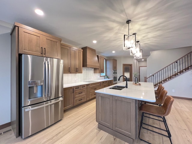 kitchen with custom exhaust hood, decorative light fixtures, light hardwood / wood-style flooring, a center island with sink, and stainless steel appliances