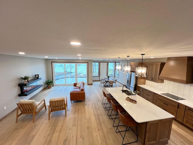 kitchen with premium range hood, sink, decorative light fixtures, black electric stovetop, and a large island