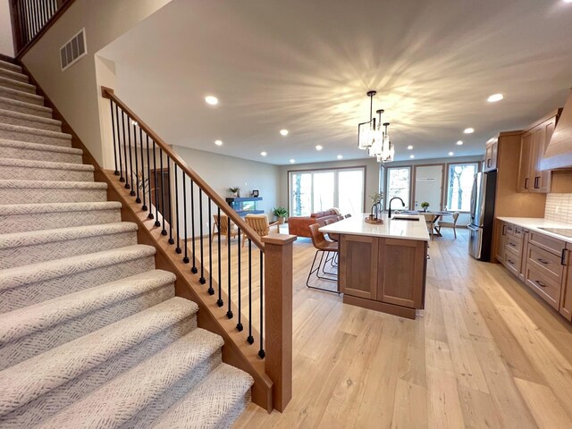 kitchen featuring sink, stainless steel fridge, hanging light fixtures, a center island with sink, and light hardwood / wood-style flooring