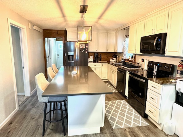 kitchen with dark wood-type flooring, decorative light fixtures, a textured ceiling, a kitchen island, and black appliances