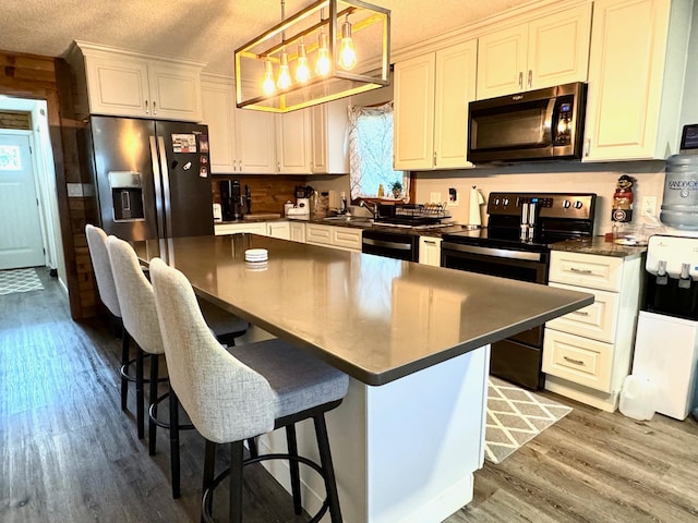 kitchen featuring a breakfast bar area, black appliances, white cabinets, a kitchen island, and decorative light fixtures