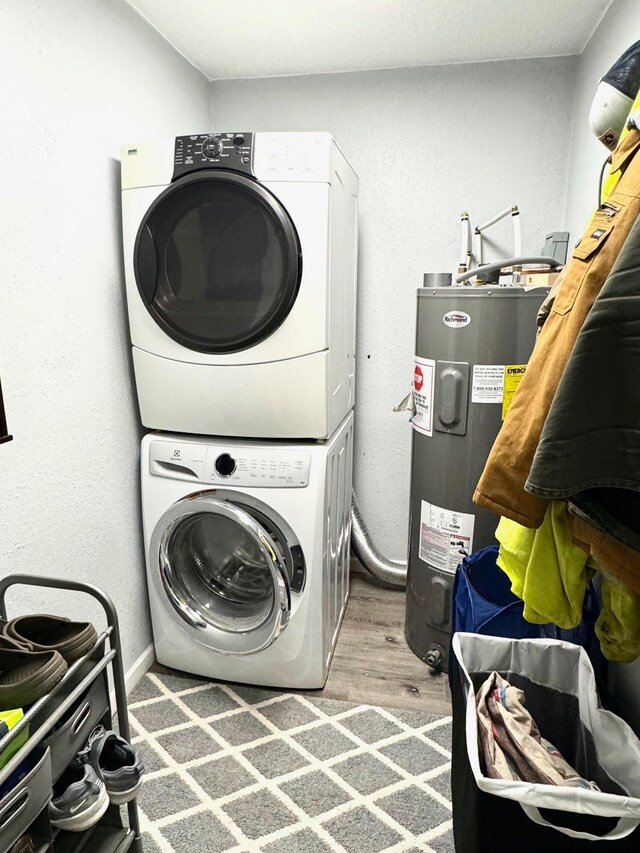 laundry area with wood-type flooring, stacked washer / drying machine, and water heater