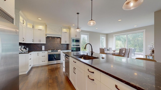 kitchen with sink, white cabinetry, hanging light fixtures, dark stone countertops, and appliances with stainless steel finishes