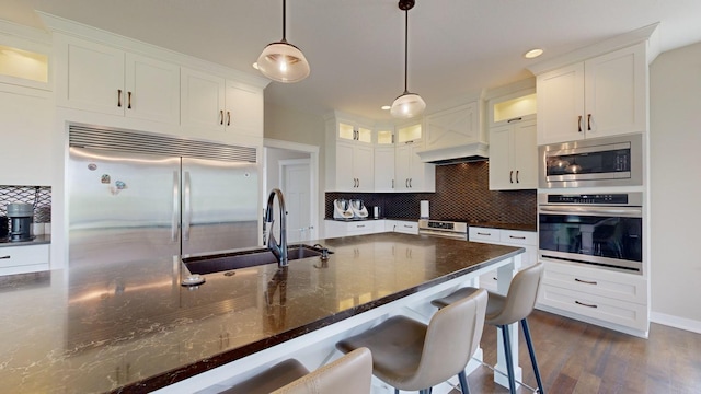 kitchen with built in appliances, sink, pendant lighting, and white cabinetry