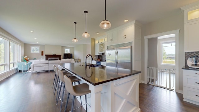 kitchen with sink, built in refrigerator, an island with sink, decorative backsplash, and white cabinets