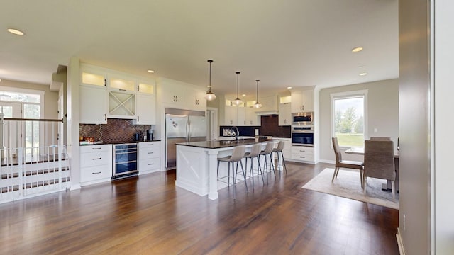 kitchen featuring wine cooler, a kitchen bar, white cabinetry, built in appliances, and a center island with sink