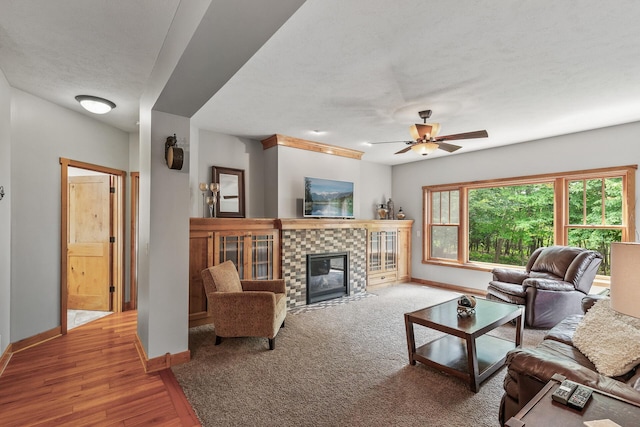 living area featuring a ceiling fan, wood finished floors, baseboards, a fireplace, and a textured ceiling