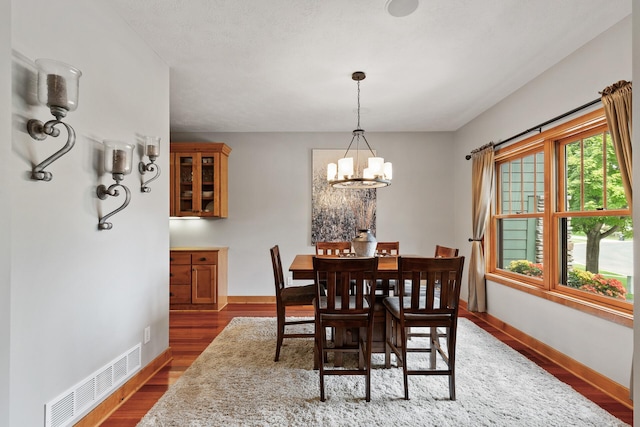 dining area featuring a chandelier, visible vents, baseboards, and wood finished floors