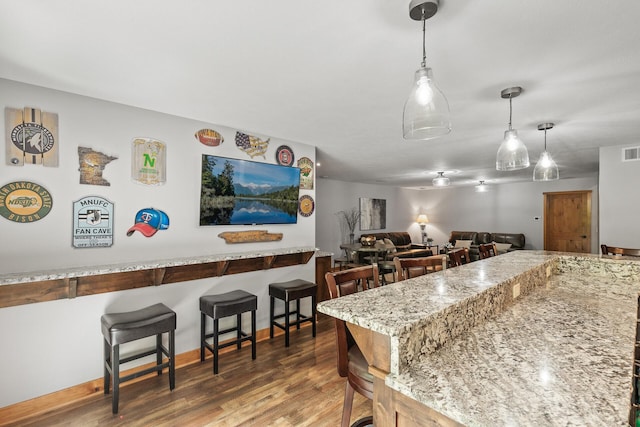 kitchen with decorative light fixtures, visible vents, a breakfast bar, and wood finished floors