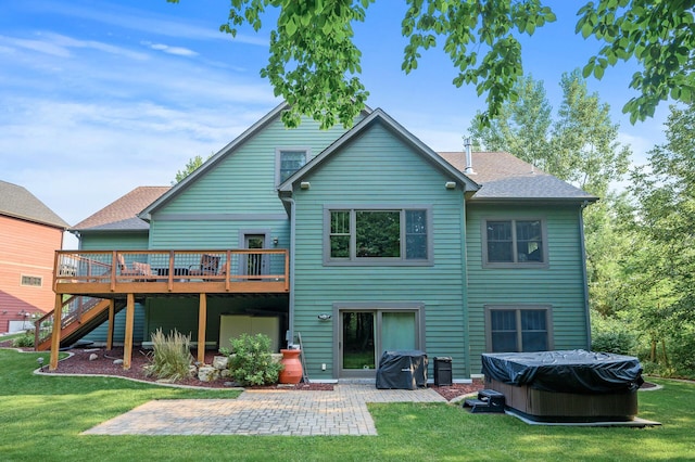 rear view of property with a hot tub, a wooden deck, roof with shingles, a lawn, and a patio area