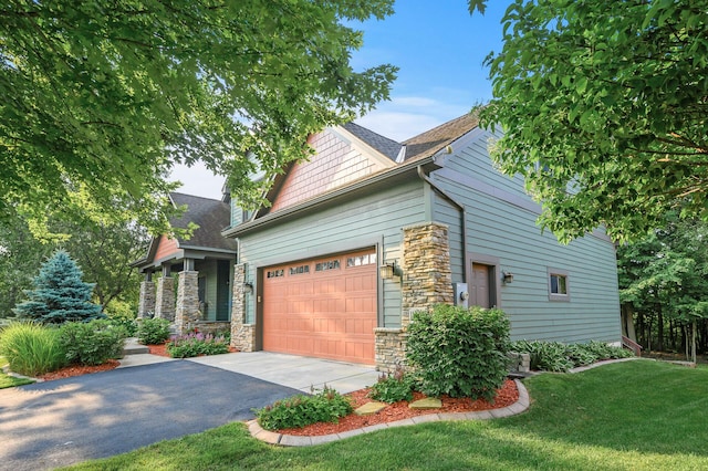 view of side of property with a garage, stone siding, a lawn, and driveway