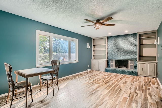 dining area with ceiling fan, a textured ceiling, light wood-type flooring, and a brick fireplace