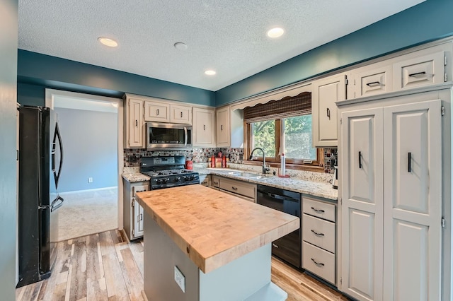 kitchen with a kitchen island, butcher block counters, light wood-type flooring, black appliances, and sink