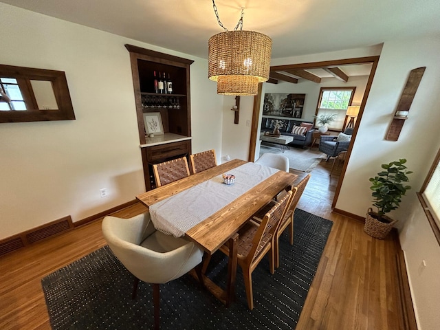 dining room featuring baseboards, visible vents, wood finished floors, beam ceiling, and a notable chandelier