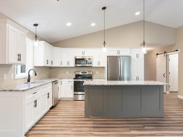 kitchen with stainless steel appliances, sink, a barn door, a kitchen island, and light hardwood / wood-style floors