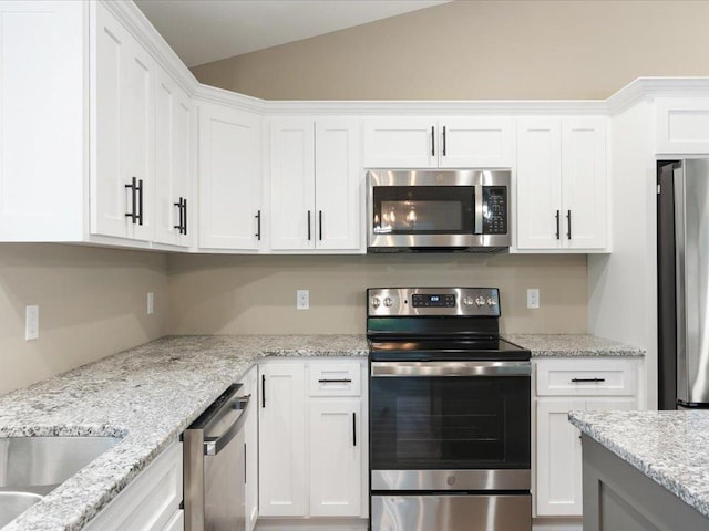 kitchen with appliances with stainless steel finishes, light stone counters, lofted ceiling, and white cabinetry