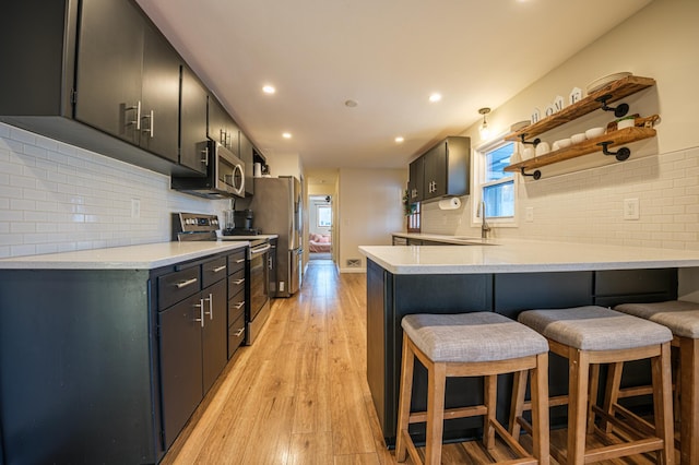 kitchen featuring a kitchen breakfast bar, appliances with stainless steel finishes, light wood-type flooring, kitchen peninsula, and decorative backsplash