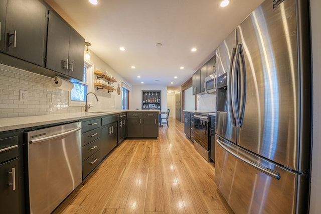 kitchen featuring appliances with stainless steel finishes, light wood-type flooring, pendant lighting, sink, and tasteful backsplash