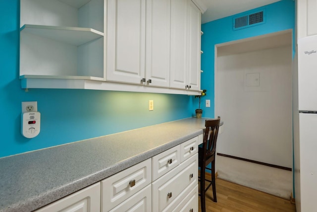 interior space with light wood-type flooring, white refrigerator, and white cabinetry