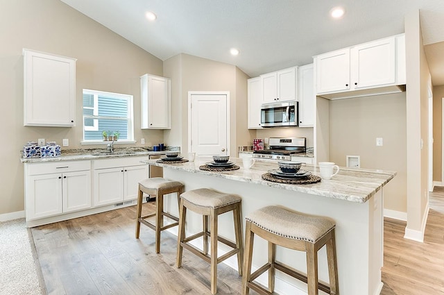 kitchen with a kitchen island, gas range, light stone countertops, vaulted ceiling, and white cabinetry