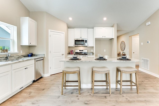 kitchen featuring light stone countertops, appliances with stainless steel finishes, light wood-type flooring, a center island, and white cabinets