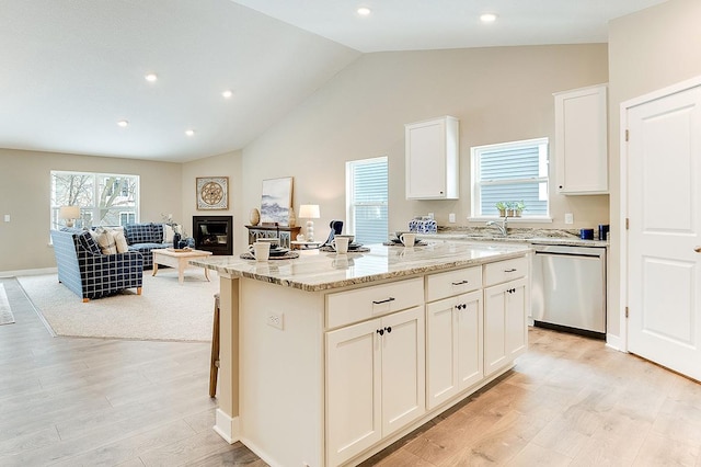 kitchen with a kitchen island, a wealth of natural light, white cabinetry, dishwasher, and light stone counters