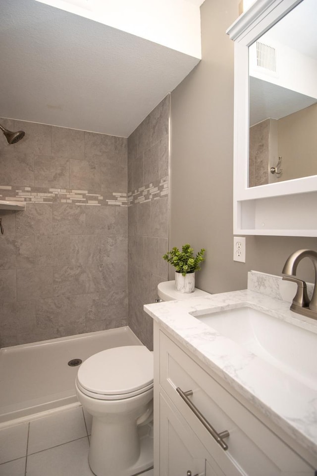 bathroom with tile patterned flooring, vanity, toilet, and a tile shower