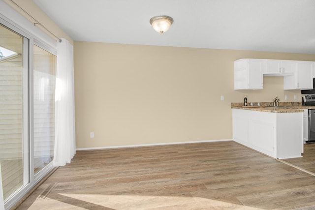 kitchen with white cabinetry, stainless steel range, light stone counters, sink, and light hardwood / wood-style floors