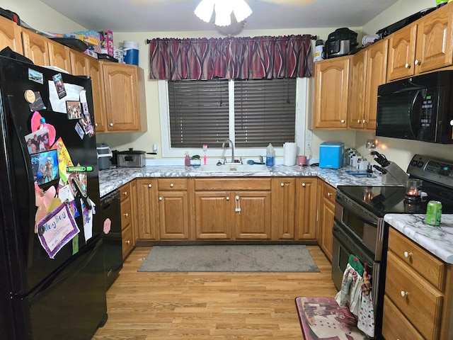 kitchen with black appliances, light stone countertops, sink, and light hardwood / wood-style floors