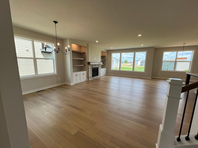 unfurnished living room with built in shelves, light hardwood / wood-style flooring, and an inviting chandelier