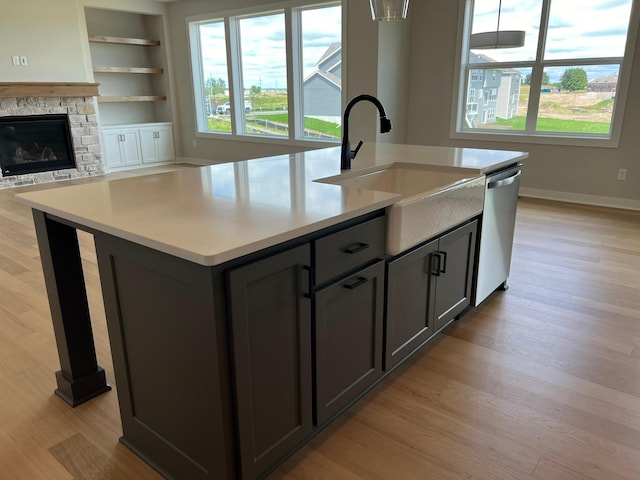 kitchen with built in shelves, sink, light hardwood / wood-style flooring, dishwasher, and an island with sink