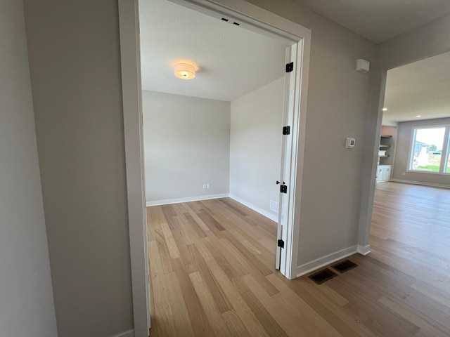 hall with a textured ceiling and light hardwood / wood-style floors