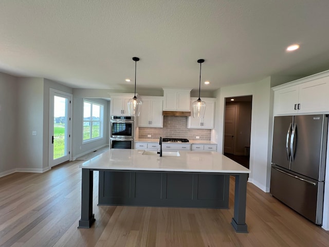 kitchen with sink, a center island with sink, hanging light fixtures, stainless steel appliances, and white cabinets