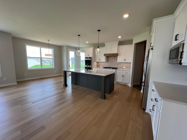 kitchen featuring decorative light fixtures, white cabinetry, a kitchen island with sink, stainless steel appliances, and custom range hood