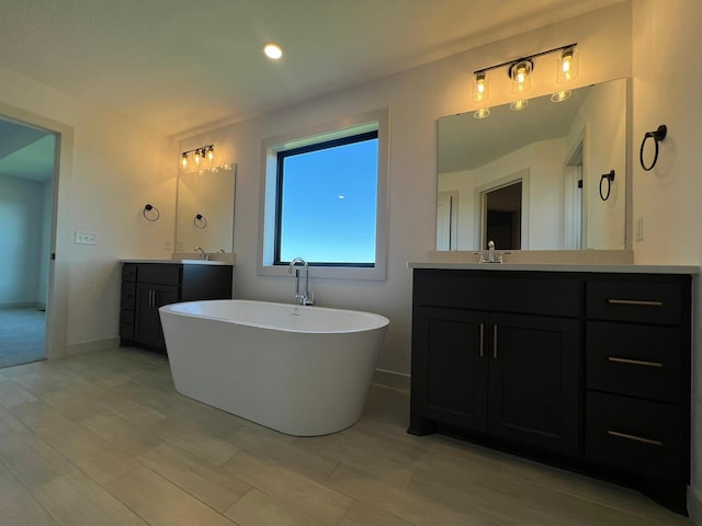 bathroom with a soaking tub, wood finished floors, a sink, and two vanities