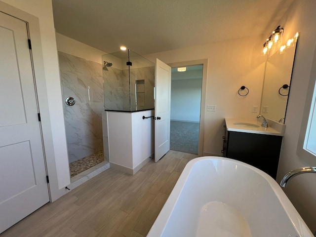 full bathroom featuring wood finished floors, a freestanding tub, vanity, and a marble finish shower