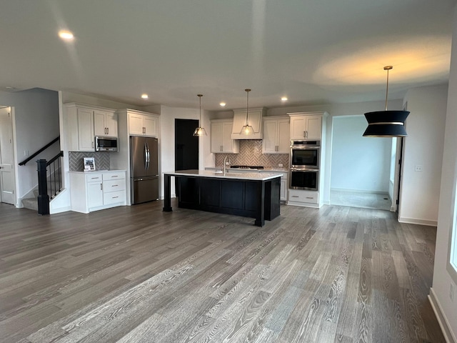 kitchen with white cabinetry, appliances with stainless steel finishes, hanging light fixtures, and a center island with sink