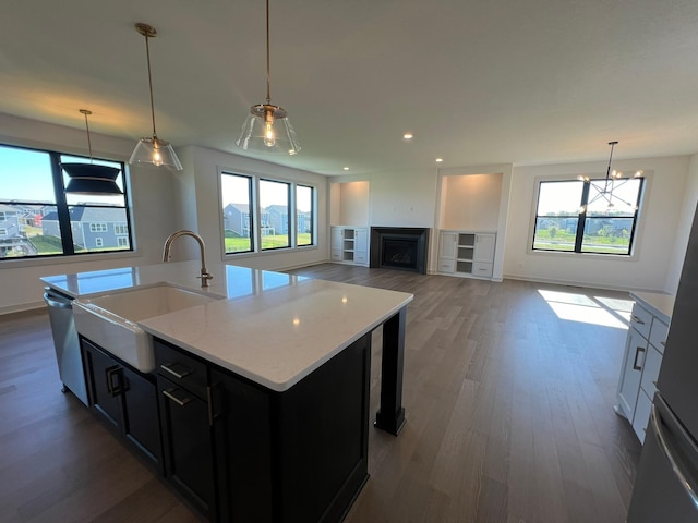 kitchen with a kitchen island with sink, sink, decorative light fixtures, and dark wood-type flooring