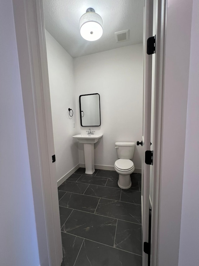bathroom with a textured ceiling, marble finish floor, baseboards, toilet, and visible vents