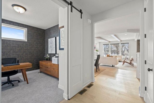 office with a barn door, visible vents, baseboards, a textured ceiling, and light wood-style floors