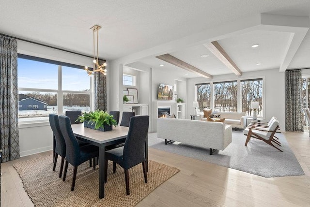 dining room with light wood-type flooring, a glass covered fireplace, a healthy amount of sunlight, and beamed ceiling