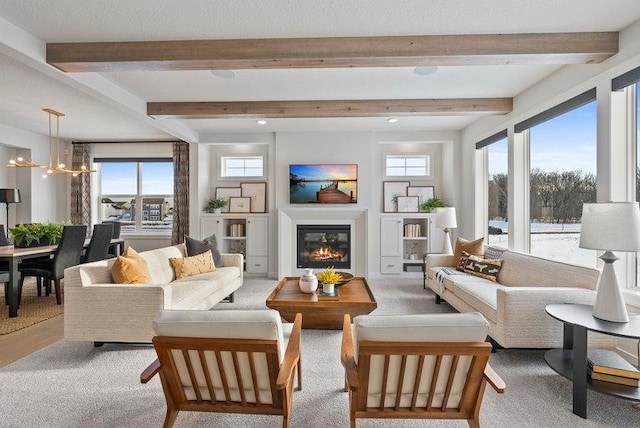 interior space with beamed ceiling, a glass covered fireplace, a wealth of natural light, and a notable chandelier