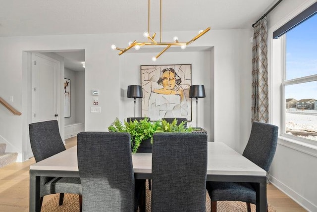 dining room featuring light wood finished floors, baseboards, stairway, and a chandelier