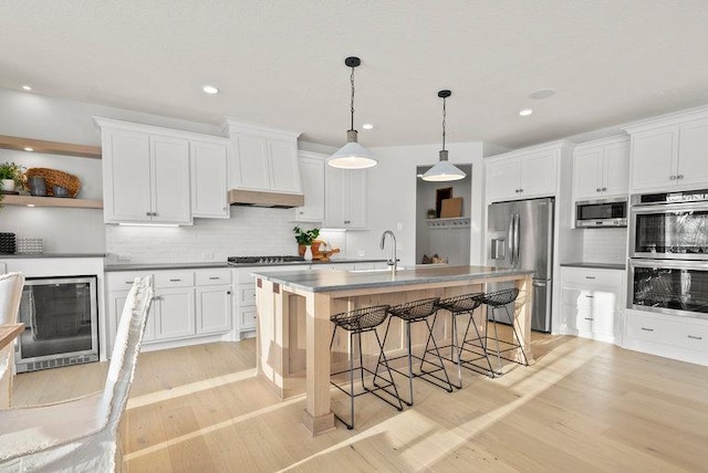 kitchen with light wood-style flooring, a breakfast bar, stainless steel appliances, open shelves, and a sink