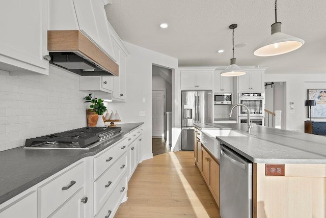 kitchen featuring backsplash, appliances with stainless steel finishes, light wood-style floors, a sink, and premium range hood