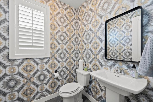 half bath featuring baseboards, a sink, toilet, and wallpapered walls