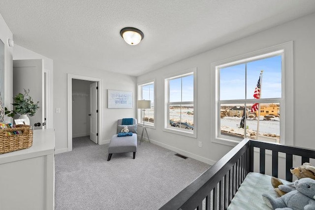 carpeted bedroom featuring a textured ceiling, a spacious closet, visible vents, and baseboards