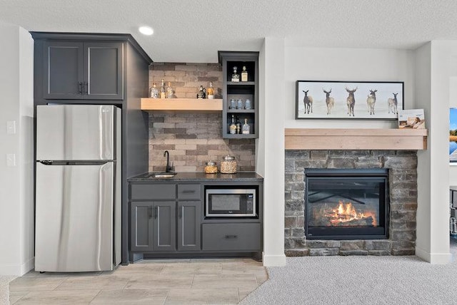 bar featuring a sink, stainless steel appliances, a textured ceiling, a stone fireplace, and indoor wet bar